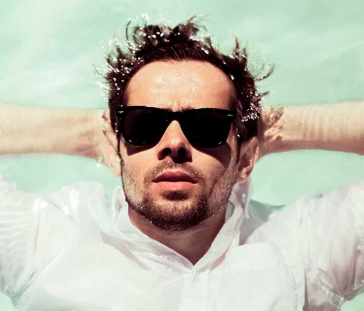 Hombre con lentes de sol recostado sobre el agua en una piscina - Homme Luxury Barbers
