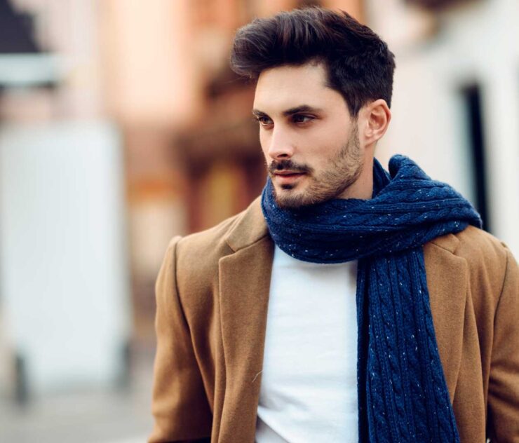 Hombre con abrigo café y bufanda azul - Homme Luxury Barbers