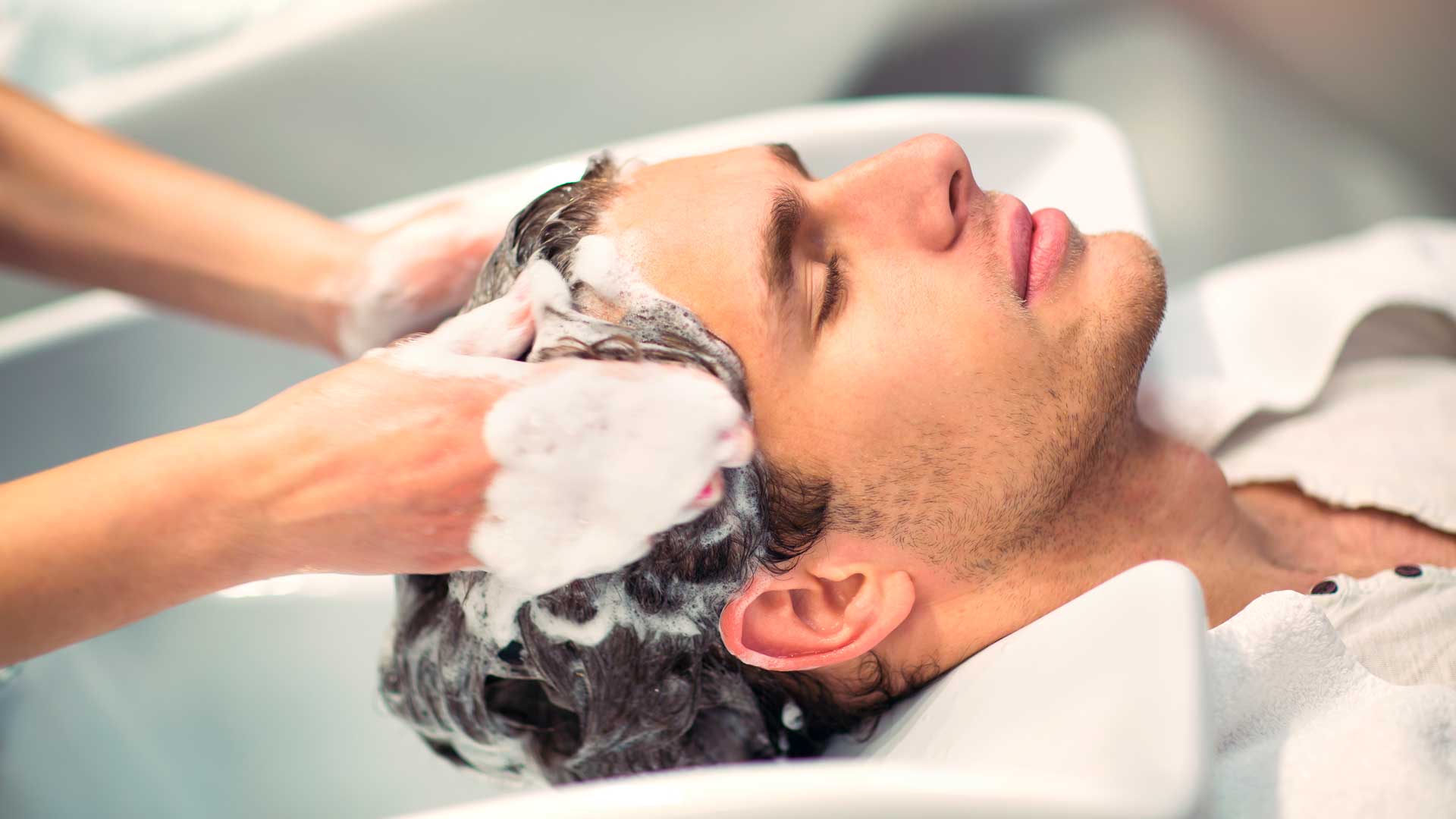 Manos lavando el cabello de un hombre.